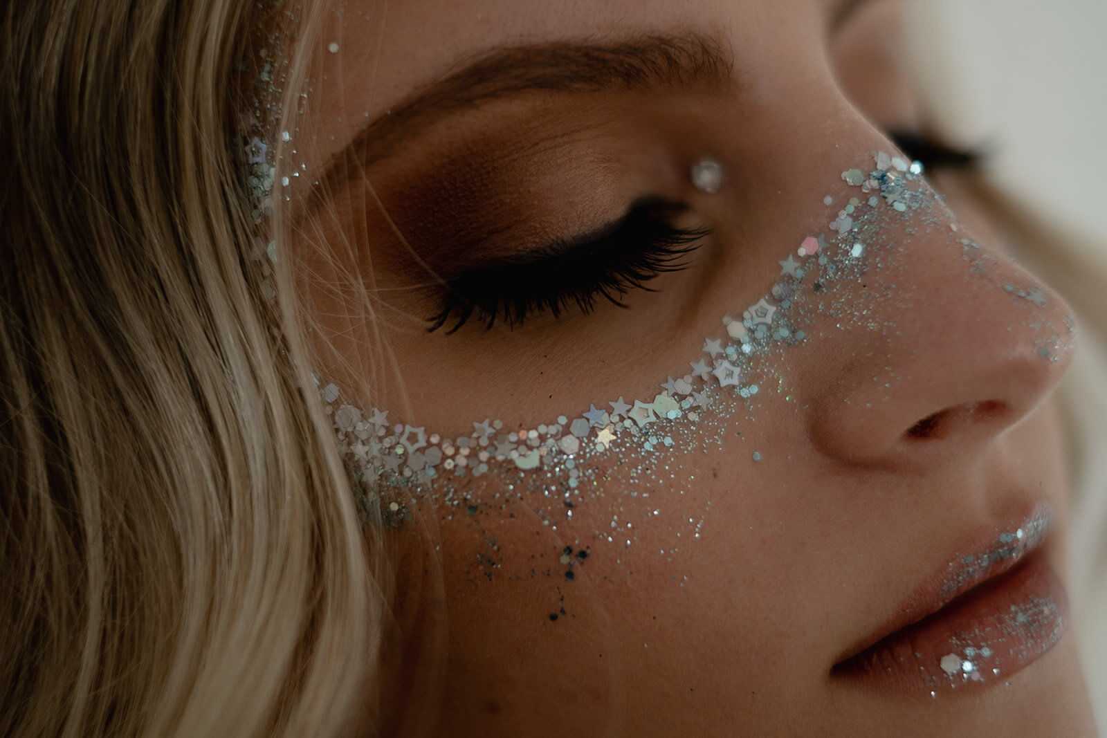 Close-up of a woman's face with glitter and star confetti makeup around her eyes and on her cheeks.