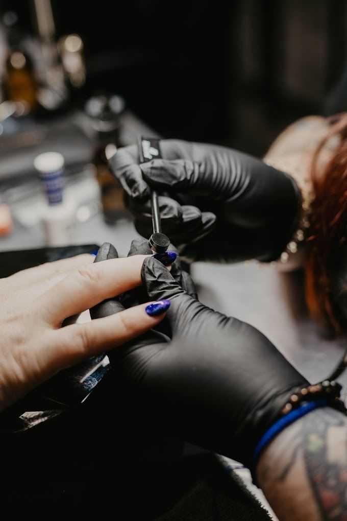 Nail artist in black gloves painting client’s nails in a salon.