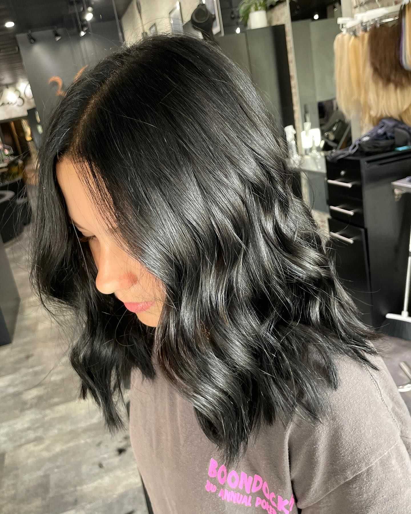 Woman with wavy, dark hair in a salon, wearing a casual brown t-shirt.