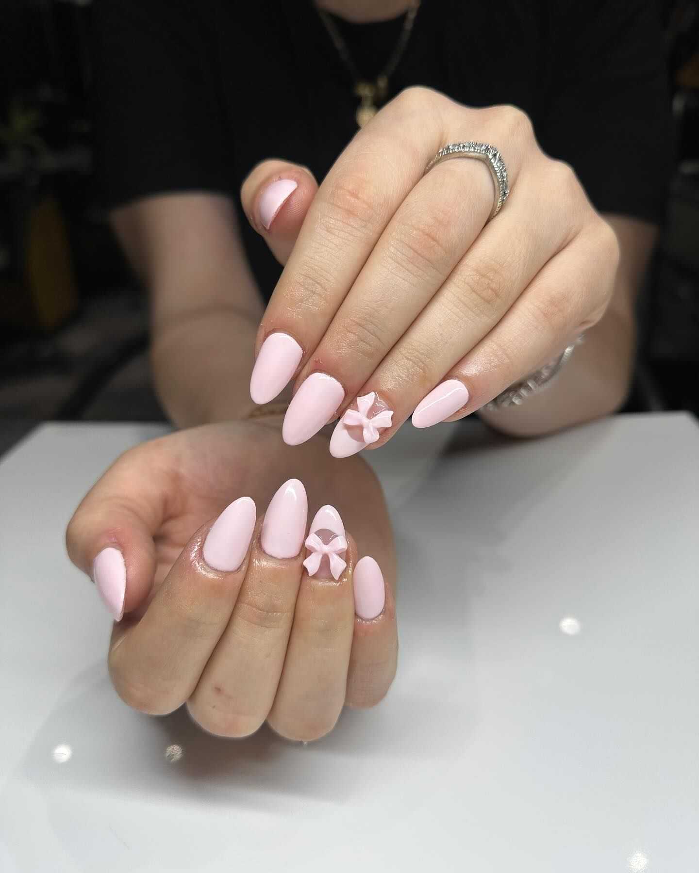 Person showing pastel pink manicured nails with a 3D floral design on the ring finger.