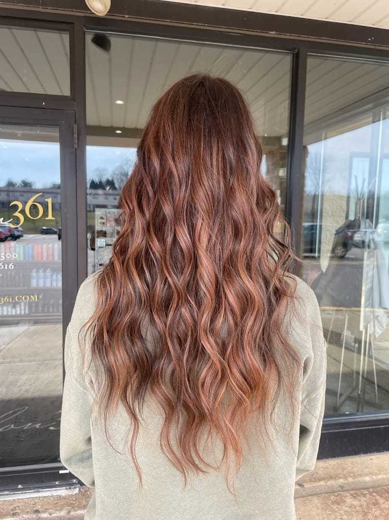 Long wavy auburn hair styled on a person wearing a green top, seen from the back.