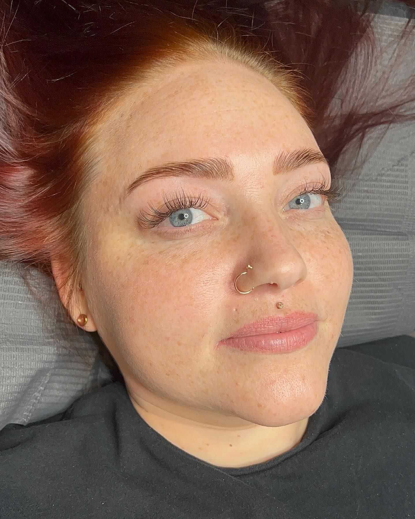 Red-haired woman with nose rings lying down, wearing a black shirt.