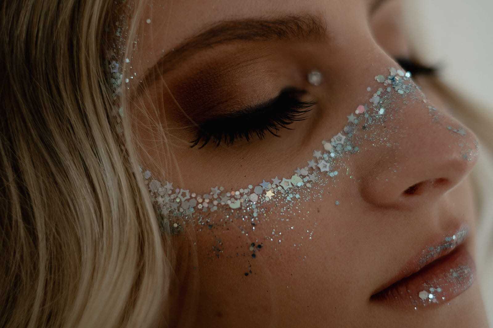 Close-up of a woman's face with glitter and star confetti makeup around her eyes and on her cheeks.